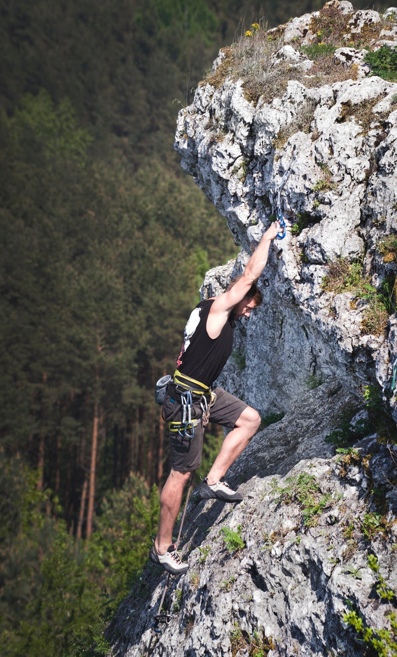 man wearing black tank top and brown shorts climbing rock